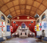 A photograph on the interior of a historic hall with a arched wooden roof at colourful flags adorning the walls