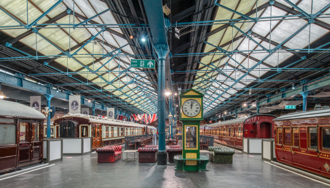 A photograph shows The National Railway Museum's Station Hall, a large building with two sloping glass roofs and an assortment of train carriages on tracks