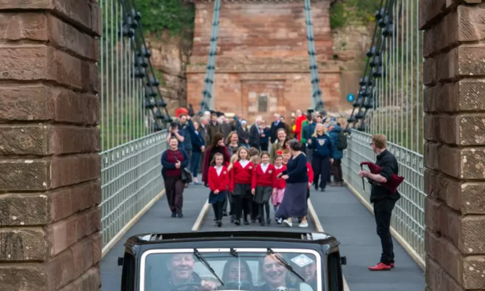 A vintage car and school children cross the Union Chain Bridge as it reopens to traffic (Northumberland County Council)